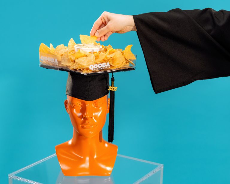 Image of grad dipping a corn chip into a queso dip on top of a graduation cap.