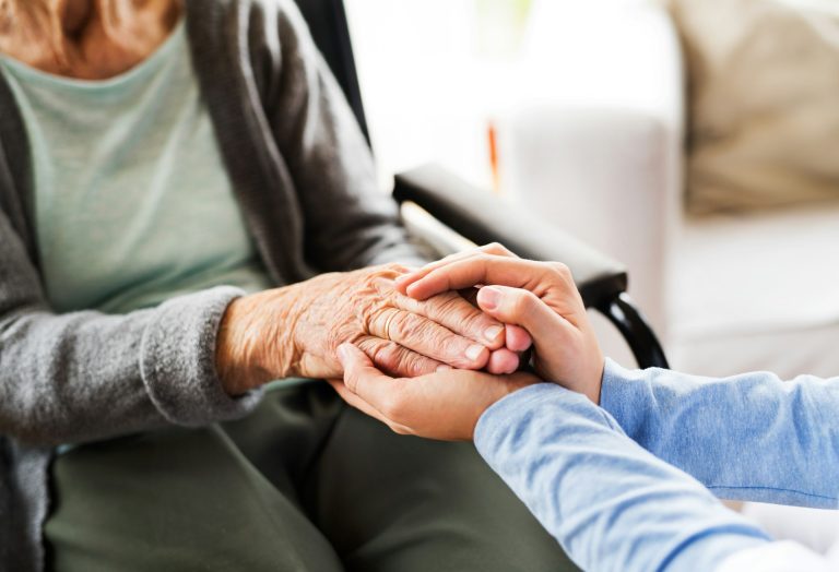 A caregiver gently holding an elderly woman’s hands in a comforting gesture, symbolizing compassion and senior care support. Franchise National Accounts Example