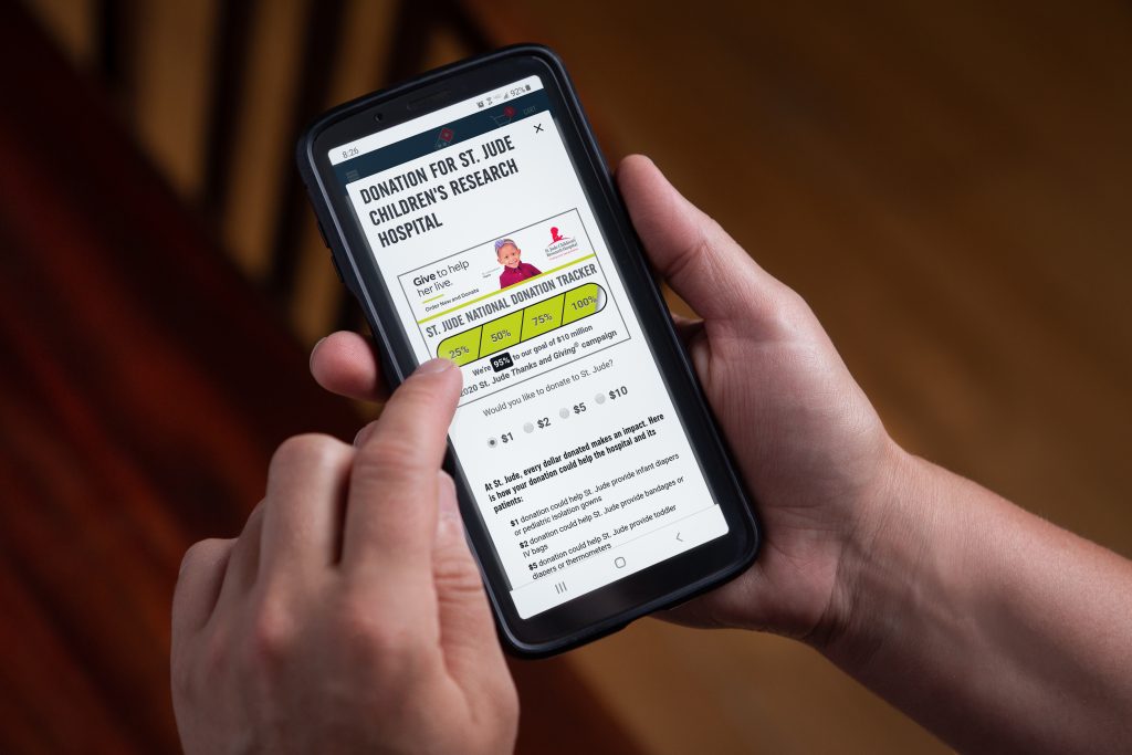 Hand using Domino’s mobile app to donate to St. Jude Children’s Research Hospital, showing donation tracker and options.