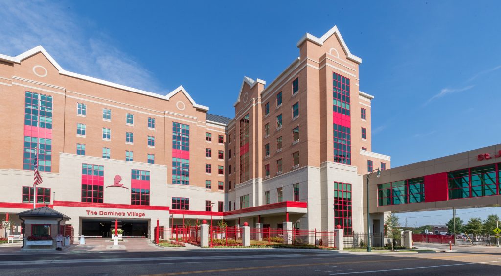 Exterior of The Domino’s Village housing facility at St. Jude, red and tan building with skybridge and American flag.