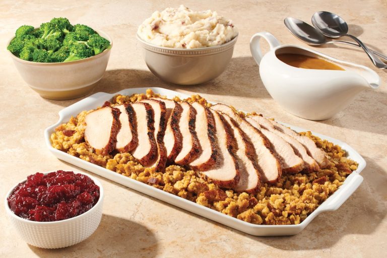 Sliced turkey over stuffing with bowls of broccoli, mashed potatoes, cranberry sauce, and gravy