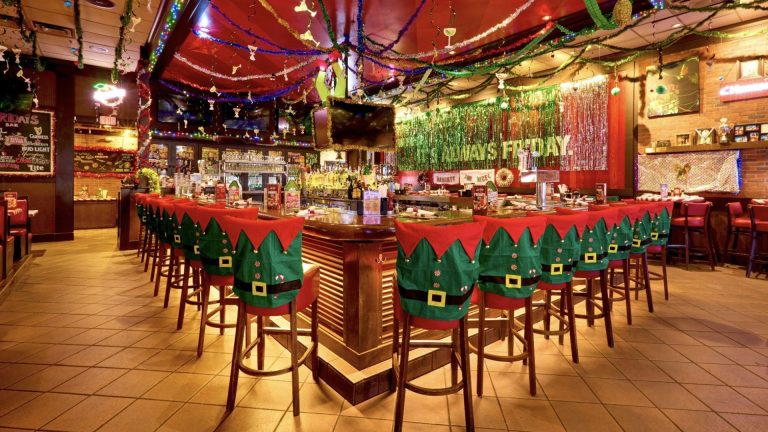 TGI Fridays bar wrapped in holiday lights with elf chair covers, tinsel, and festive menus during Elf Days takeover