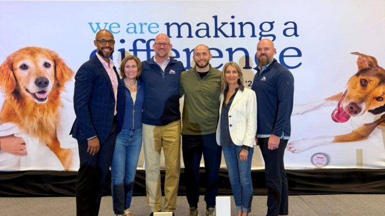 Scenthound and VMG Partners leaders stand before a “we are making a difference” backdrop with dog photos