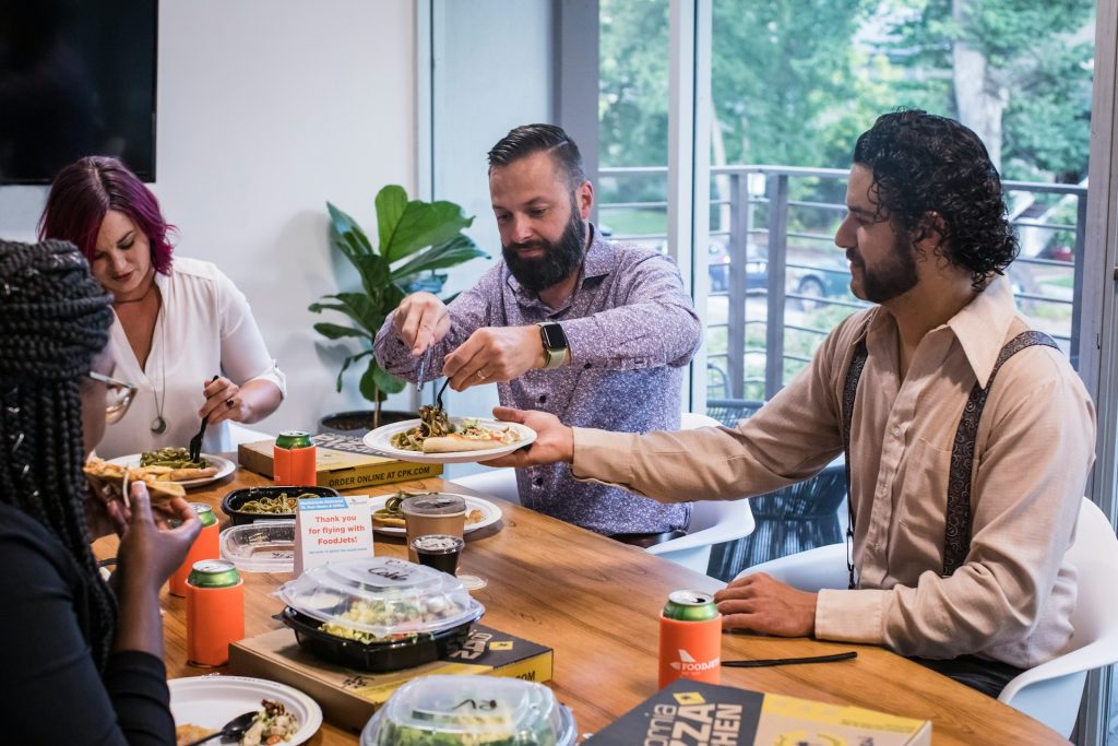 Coworkers share takeout at a conference table; casual team lunch illustrating Veterans Day restaurant offers.