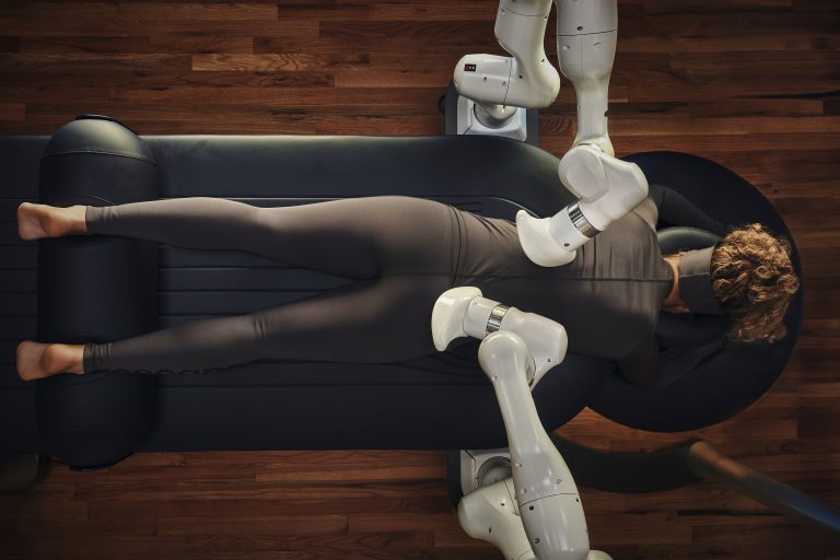Overhead view of Aescape robotic massage table using dual arms to massage a clothed guest