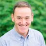 Headshot of Jim Lusardi smiling outdoors, wearing a light blue button-down shirt