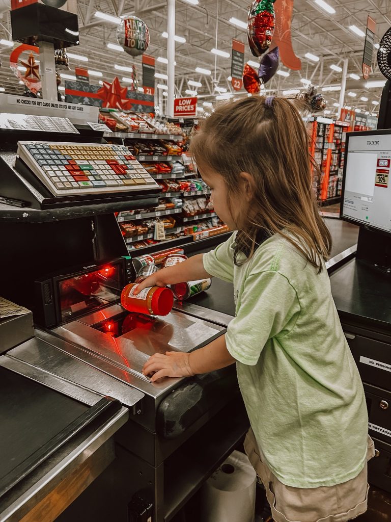 Young Primrose student scans canned goods at a grocery checkout during the Caring and Giving Food Drive