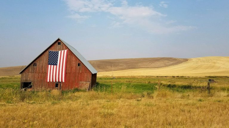 Red barn with a large American flag in a rural field under a blue sky