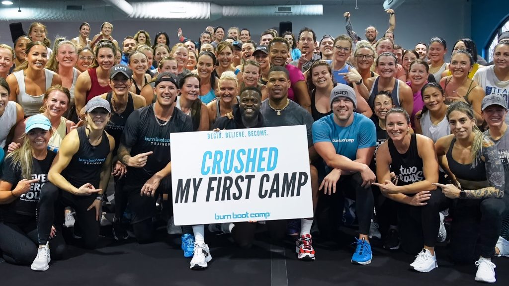 Kevin Hart holds a “Crushed My First Camp” sign with Burn Boot Camp members after a workout