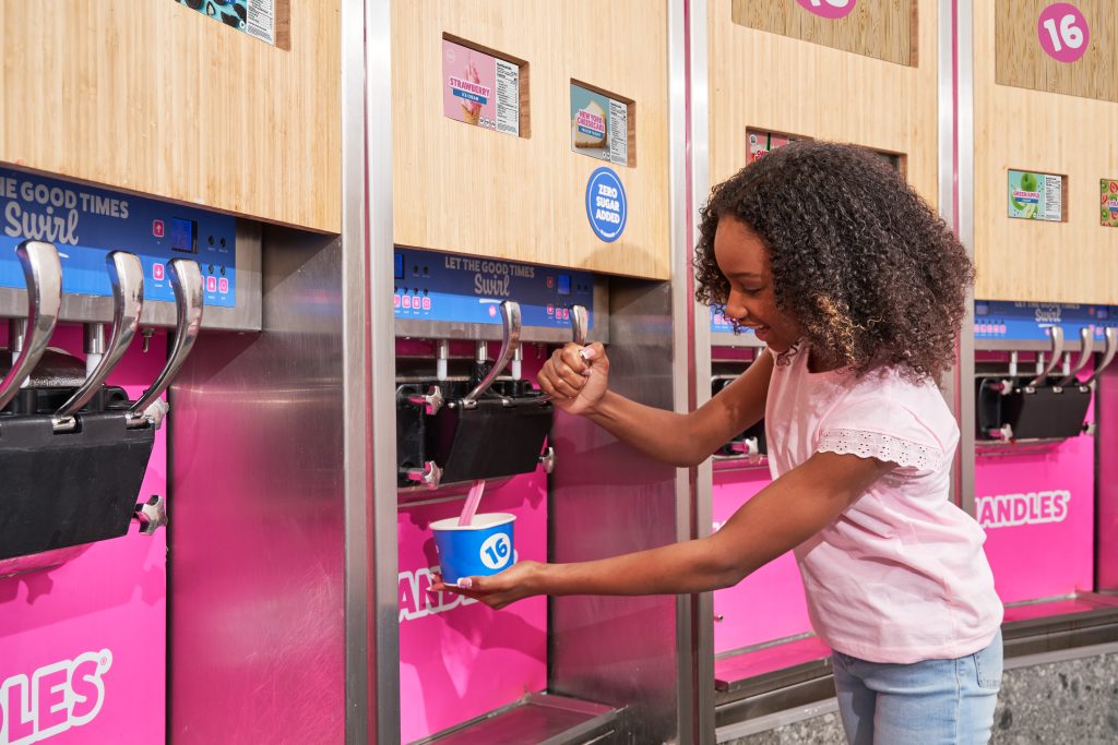 Young girl self-serving frozen yogurt at a 16 Handles soft serve machine inside a bright pink branded store