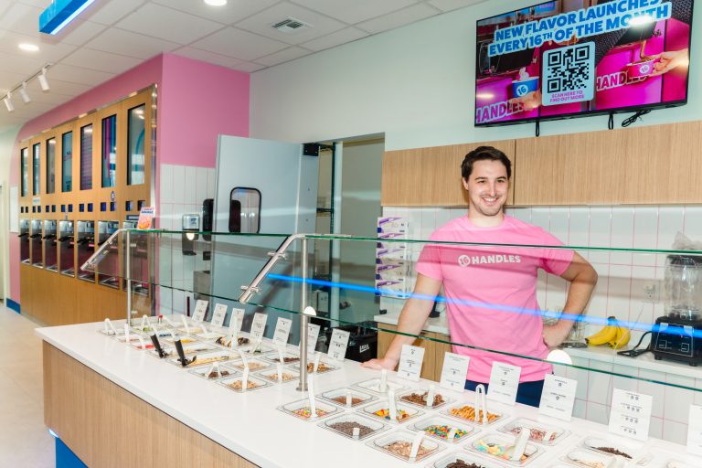 16 Handles CEO Neil Hershman smiling behind the topping bar inside a modern 16 Handles store location