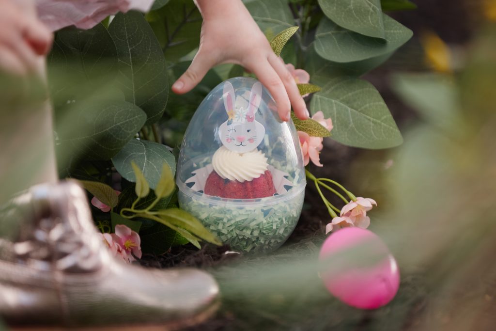 Child finding Bundtini cake inside clear Easter egg in garden