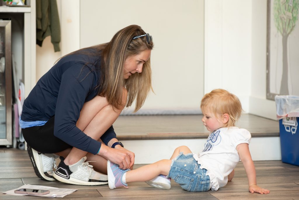 Parent helps a toddler put on a shoe at the Haven center entry