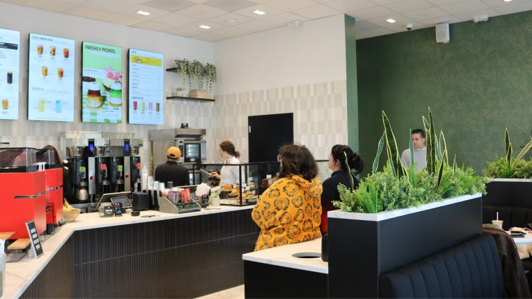 Gregorys Coffee Launches Franchise Program Customers order at a Gregorys Coffee café counter beneath digital menu boards and espresso equipment.