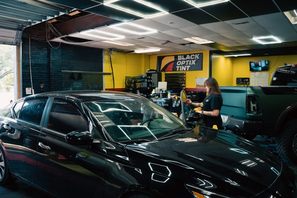 Black Optix Tint technician working on a vehicle window inside a fully branded franchise service bay