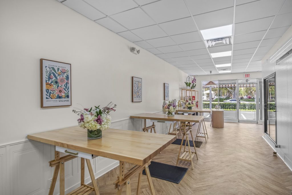 The bright and airy production workspace inside a French Florist franchise location featuring wooden design tables, herringbone floors, and fresh floral arrangements.