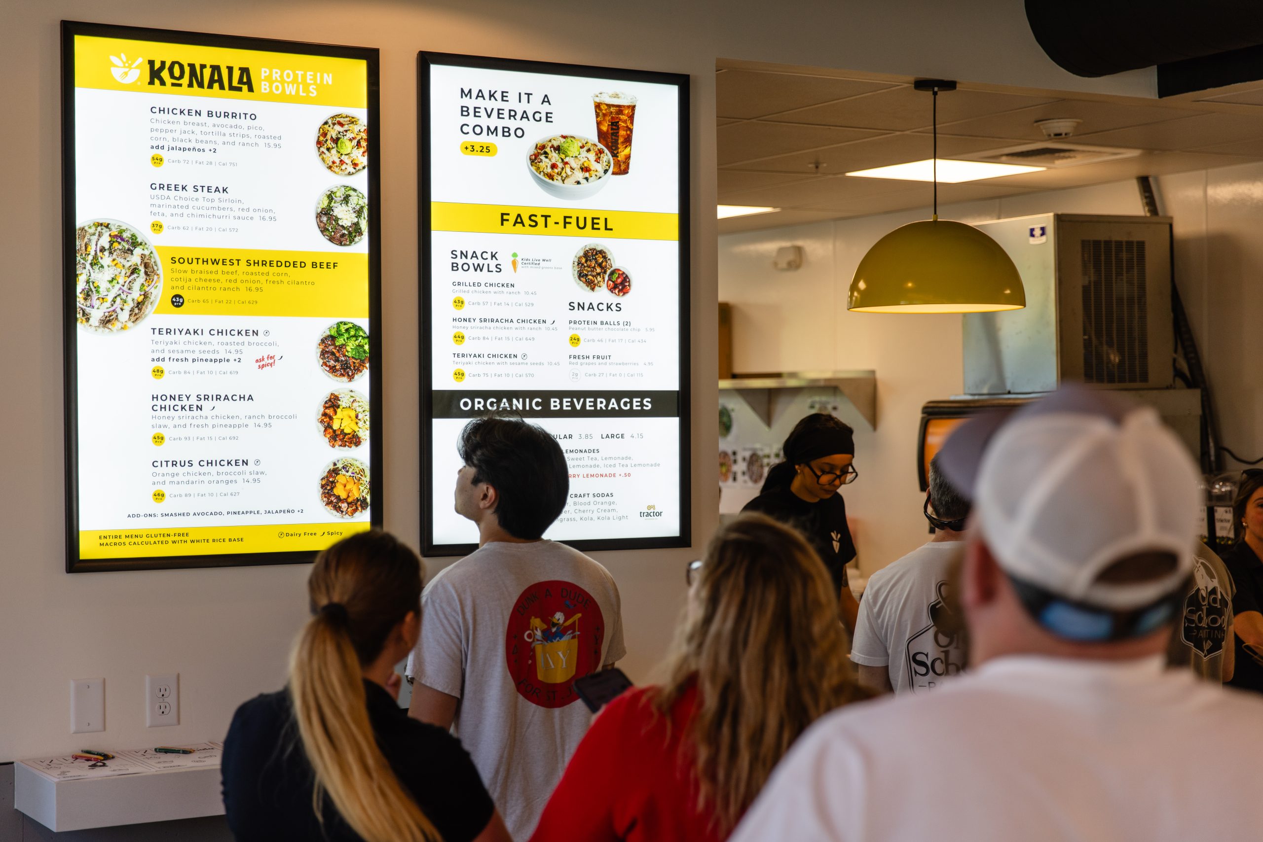 Customers ordering at the counter inside a Konala location while viewing the full menu board display