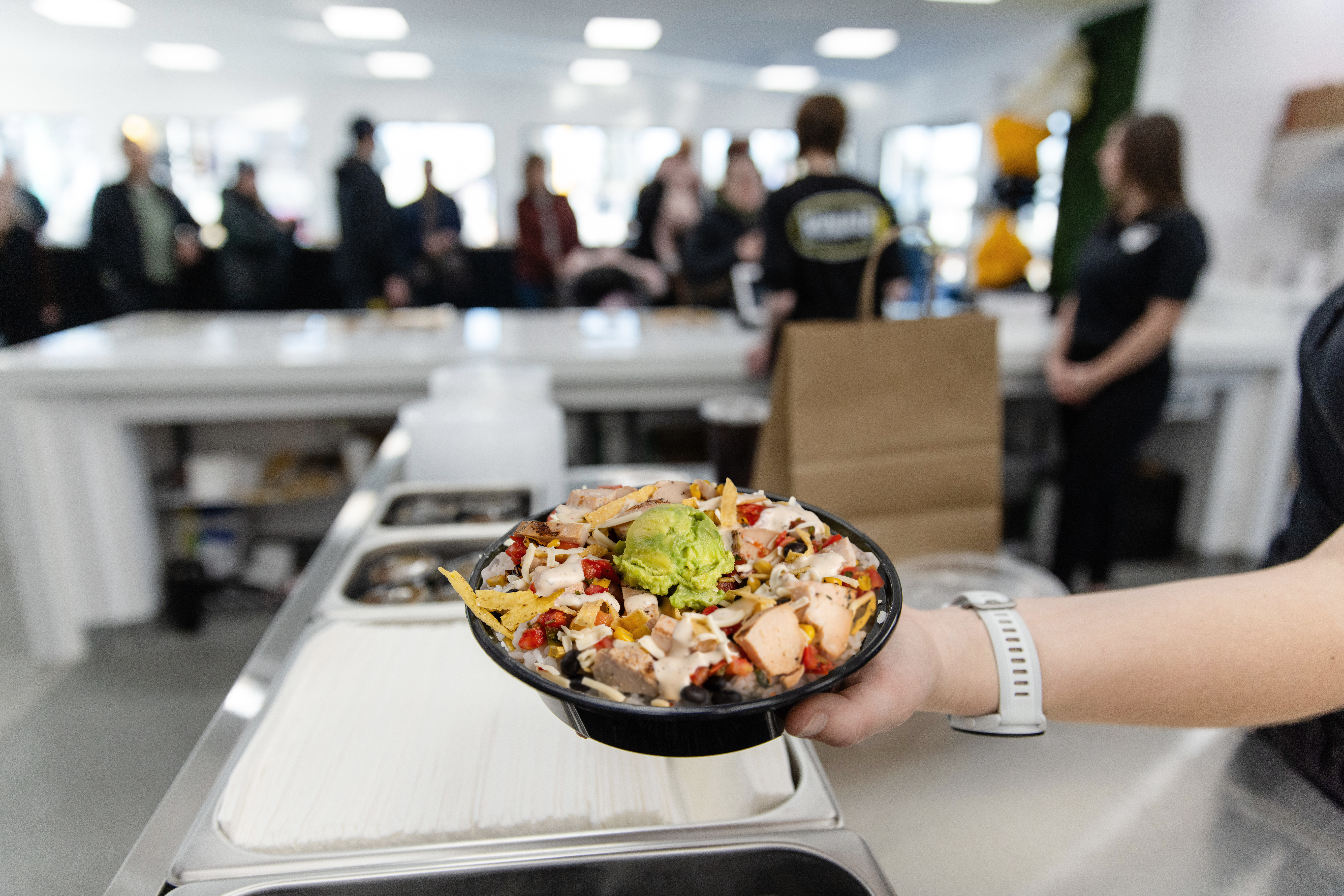Konala chicken burrito bowl with guacamole held up inside a busy Konala location during an event