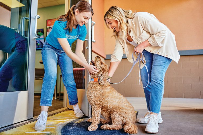Dogtopia employee greeting a dog and pet parent at daycare entrance