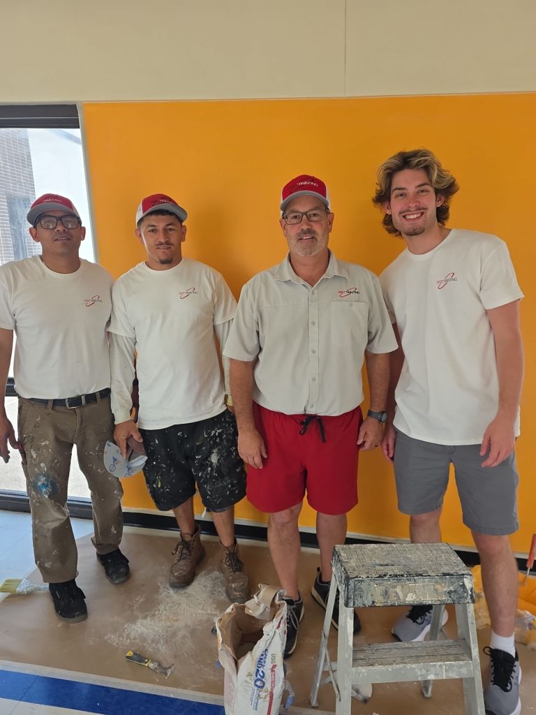 360 Painting of Kansas City crew standing together after painting a school hallway wall bright orange