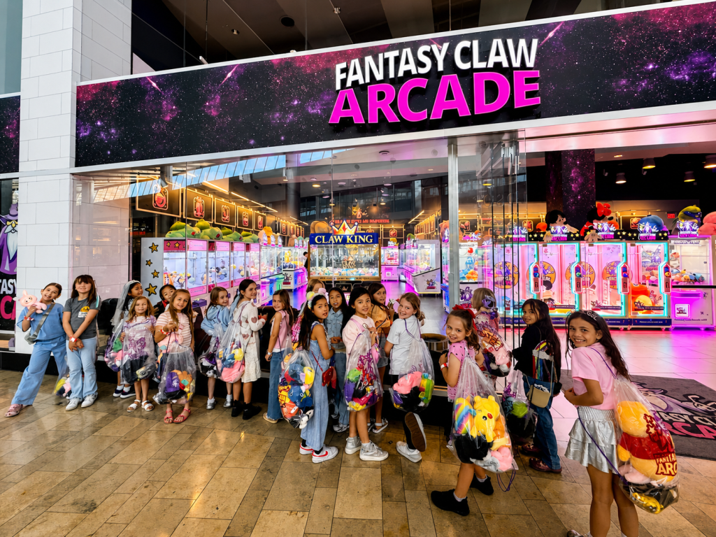 Large group of girls holding prize bags outside Fantasy Claw Arcade storefront after a birthday party
