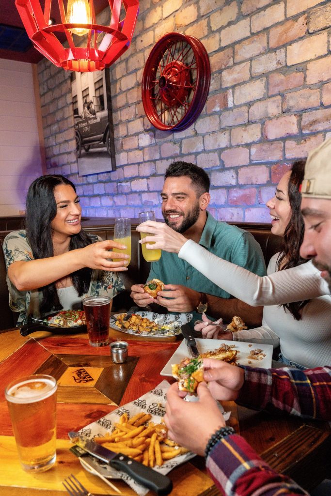 Friends toasting drinks and sharing appetizers in a Ford's Garage dining booth