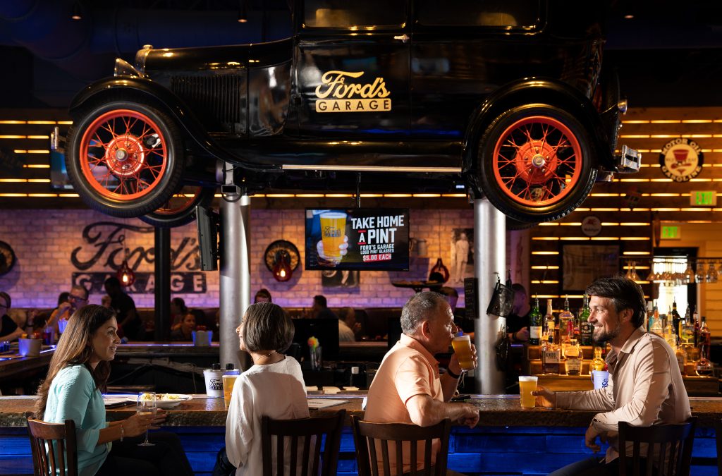 Guests enjoying drinks at the Ford's Garage bar beneath a vintage Model T