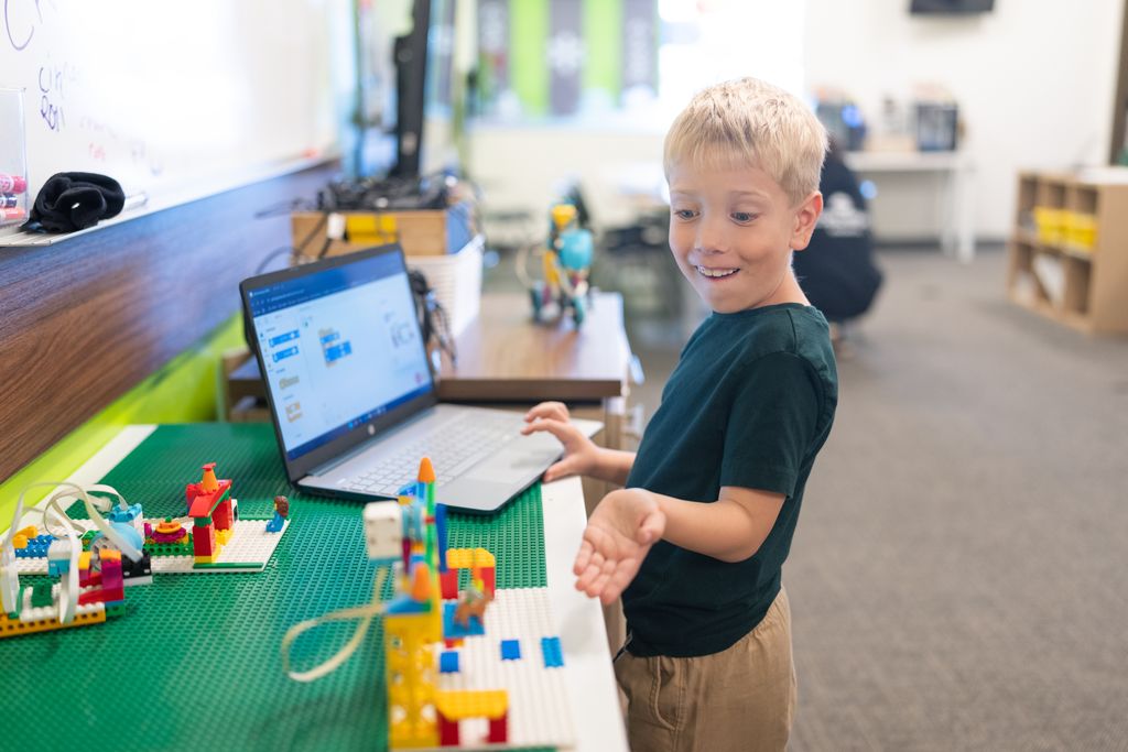 A boy reacts with excitement to a block-based coding project on a laptop at Code Ninjas.