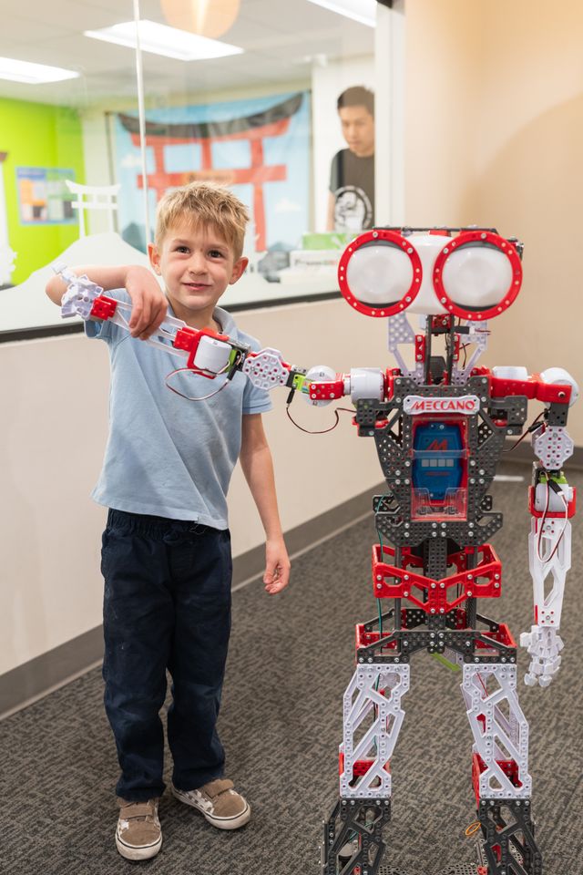 A boy poses next to a large robotics build in a Code Ninjas hallway.