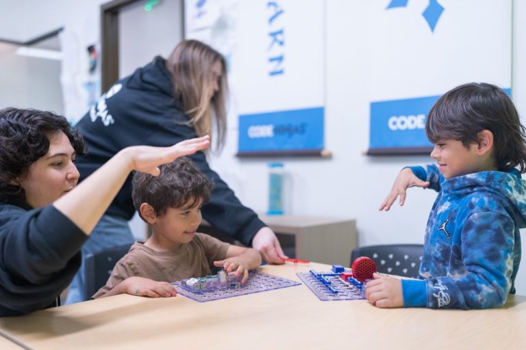 Two kids build snap circuit projects at a Code Ninjas dojo table while staff members help and high-five.