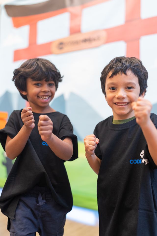Two boys in Code Ninjas t-shirts pose with playful martial arts fists in front of a dojo backdrop.