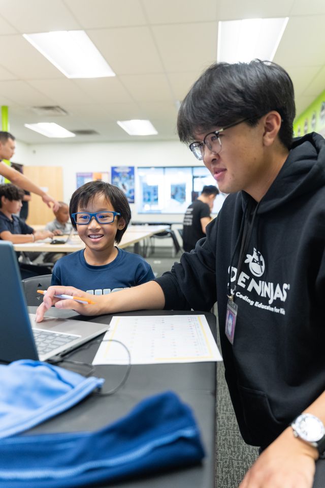 A Code Ninjas instructor guides a young student through a coding project on a laptop.