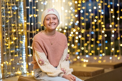 Domino’s and St. Jude Invite Customers to Give the Greatest Gift: Time Smiling St. Jude patient wearing a white knit hat and pink sweater, surrounded by glowing holiday lights